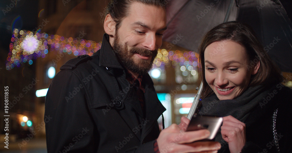 Young happy couple using smartphone at night. Young beautiful couple share memories and pictures on social media with online mobile app. Young happy couple using smartphone at night. Young beautiful couple share memories and pictures on social media with online mobile app.