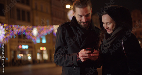 Young happy couple using smartphone at night. Young beautiful couple share memories and pictures on social media with online mobile app.