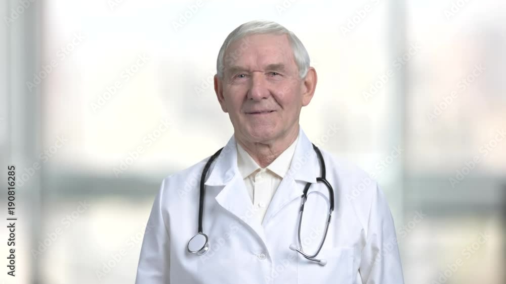 Portrait of senior doctor in abstract blurred bright background. Close up smiling old man in white coat and stethoscope. Portrait of senior doctor in abstract blurred bright background. Close up smiling old man in white coat and stethoscope.