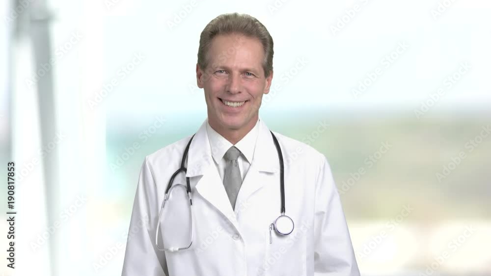 Cheerful mature male doctor smiling with teeth. Portrait of psysician man in medical suit with tie and stethoscope. Bright abstract blurred background. Cheerful mature male doctor smiling with teeth. Portrait of psysician man in medical suit with tie and stethoscope. Bright abstract blurred background.