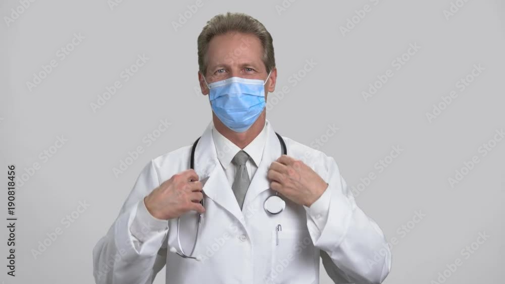 Portrait of a professional skillful doctor wear stethoscope. Mature adult handsome physician in suit and mask put on stethoscope, grey isolated background. Portrait of a professional skillful doctor wear stethoscope. Mature adult handsome physician in suit and mask put on stethoscope, grey isolated background.