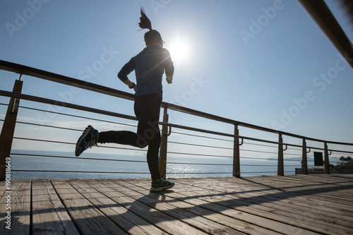 Sporty female runner running on seaside boardwalk during sunrise