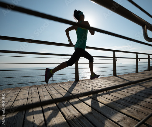 Sporty fitness female runner running on seaside boardwalk during sunrise