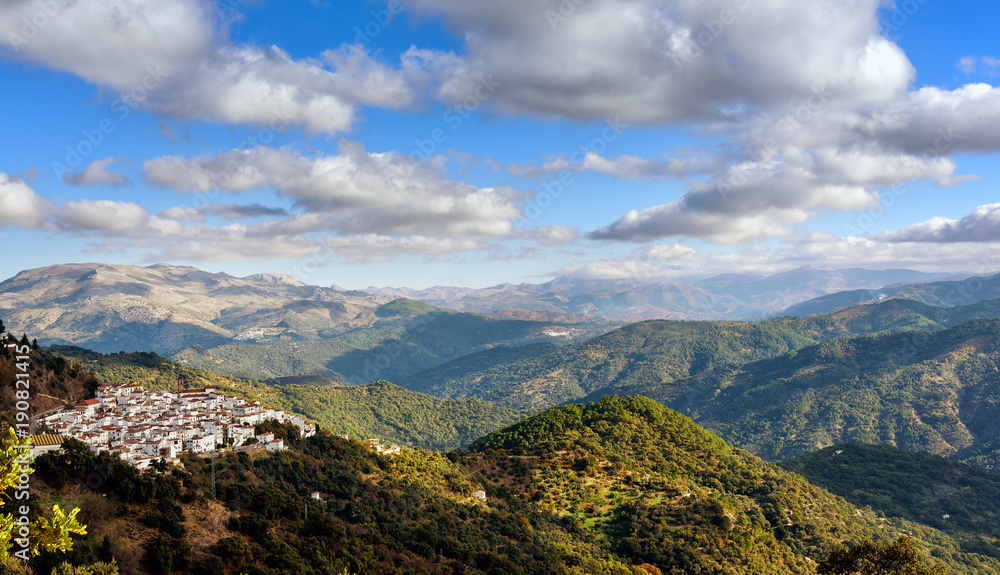 Green landscape with cloudy sky and small town among mountains in Andalusia, Spain