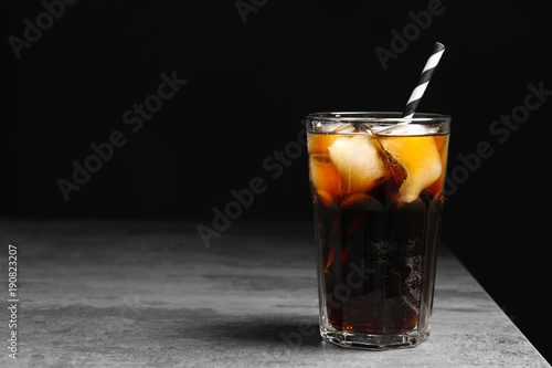 Glass of refreshing cola with ice on table against black background