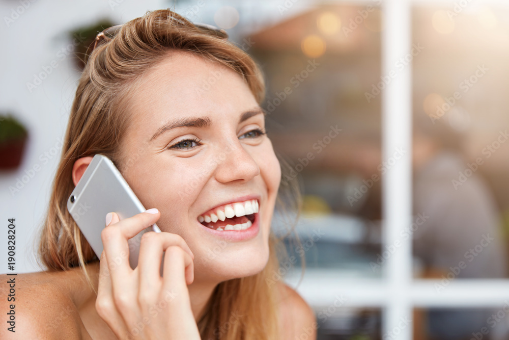 Close up portrait of overjoyed female listens funny jokes via cell phone,  laughs happily, being in good mood, expresses happiness and positiveness.  Pretty woman has broad smile during phone talk Stock Photo |