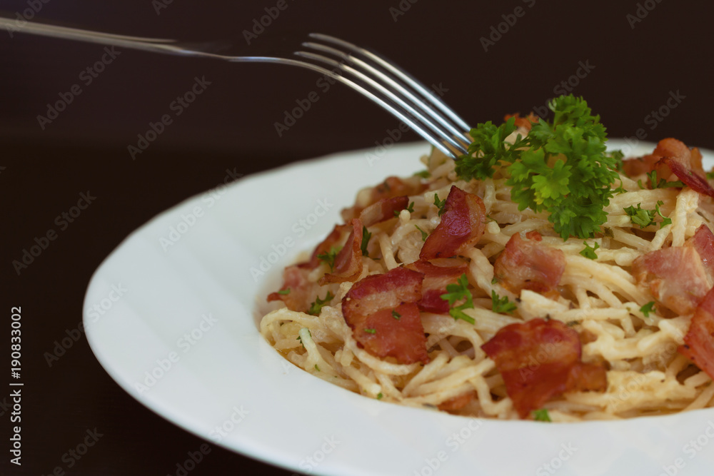 Spaghetti carbonara with bacon and cheese on white plate sprinkle with chopped parsley in close up view with copy space. Italian traditional homemade food for lunch or dinner so creamy and delicious.