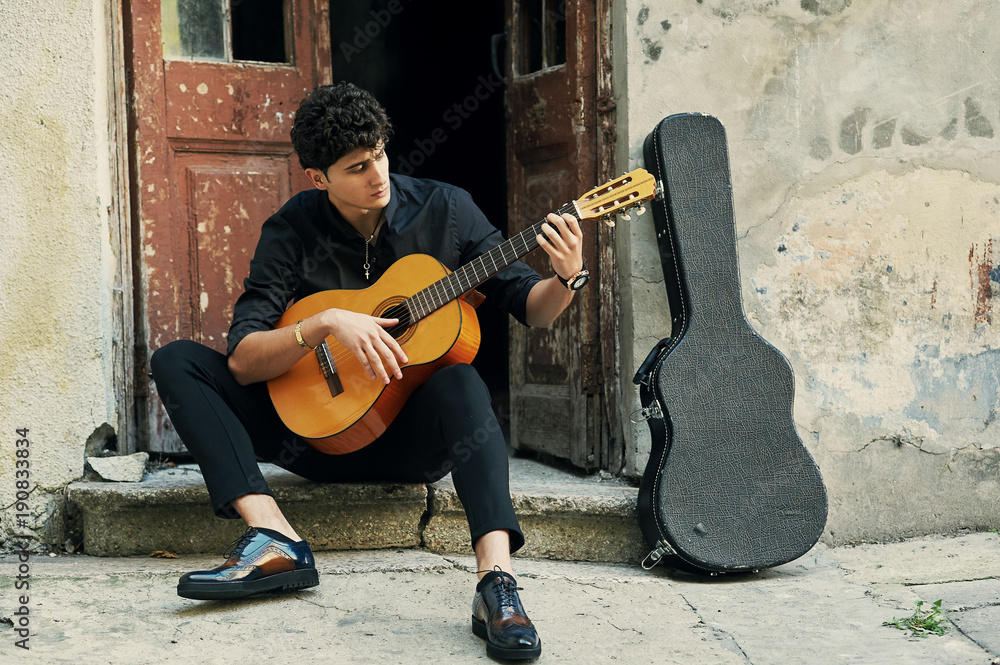 Young man playing guitar in the yard . Street musician