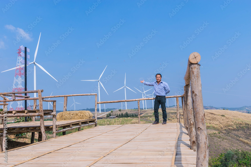 The man with viewpoint at wind turbine construction in field and meadow on the mountain with the beautiful sky cloud background at Khao Kho district, Phetchaboon province, Thailand.