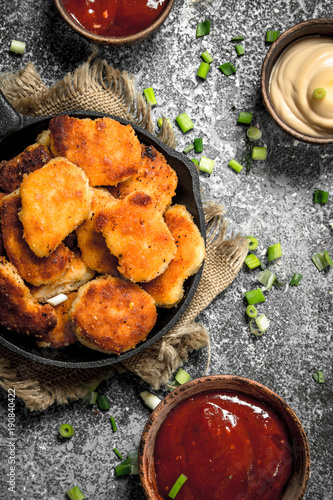 Chicken nuggets in a pan with different sauces.