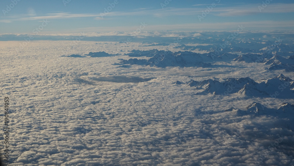 The peaks of the mountains sprout from the clouds that cover the earth. Landscape from the airplane window The peaks of the mountains sprout from the clouds that cover the earth. Landscape from the airplane window