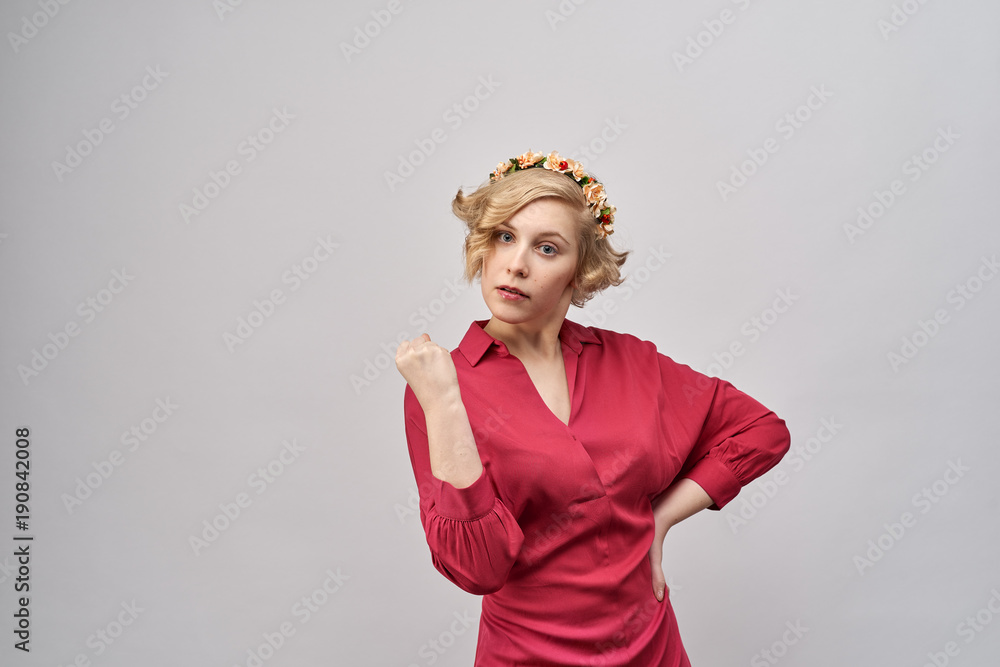 young beautiful blond woman in red dress with evil, serious , threatening expression shows her fist and threatens trouble. An annoyed expression. The concept of education, warning, admonition young beautiful blond woman in red dress with evil, serious , threatening expression shows her fist and threatens trouble. An annoyed expression. The concept of education, warning, admonition