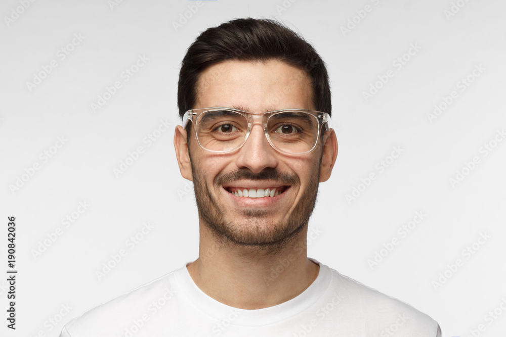 Close up shot of smiling attractive man in white t-shirt and trendy trasparent eyeglasses isolated on gray background Close up shot of smiling attractive man in white t-shirt and trendy trasparent eyeglasses isolated on gray background