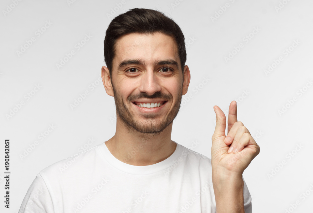 Young man with shows something tiny, smiling, shows white perfect teeth, isolated on grey background Young man with shows something tiny, smiling, shows white perfect teeth, isolated on grey background