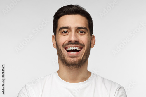 Close up horizontal shot of handsome unshaven young man in white tshirt laughing out loud, smiling broadly