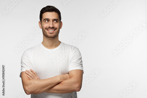 Horizontal banner with portrait of young optimistic dreamy man looking at space for your advertising text or logo, standing with crossed arms