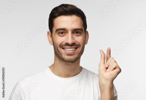 Photos Young man with shows something tiny, smiling, shows white perfect teeth, isolate