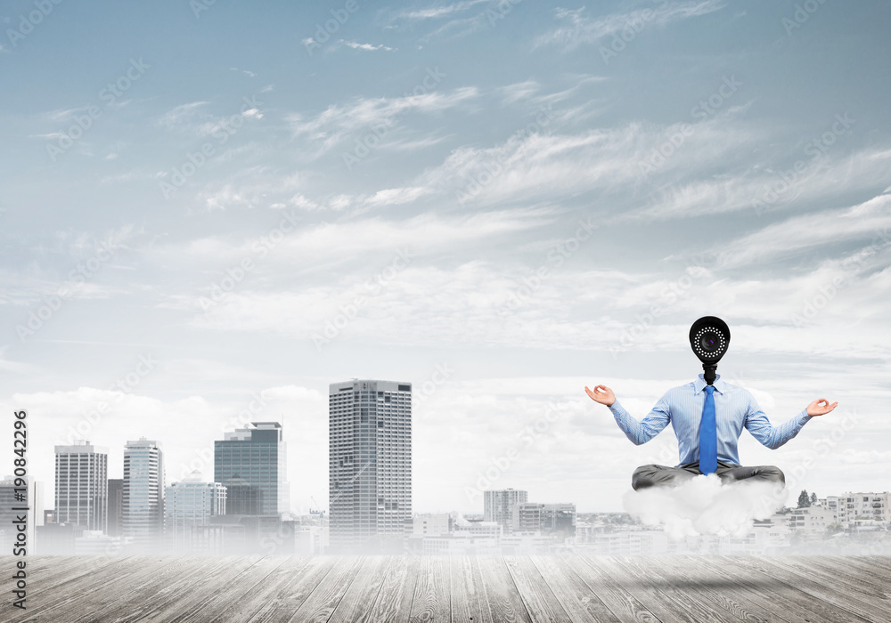 Camera headed man sitting in lotus pose on cloud against modern cityscape Camera headed man sitting in lotus pose on cloud against modern cityscape