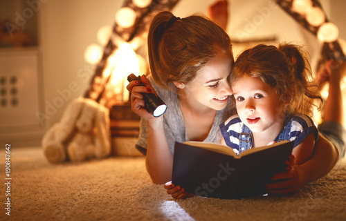 mother and child daughter with a book and a flashlight before going to bed.