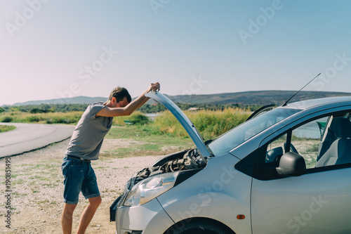 Young man looking under the hood of breakdown car outdoors. Transportation and vehicle concept © GolubaPhoto