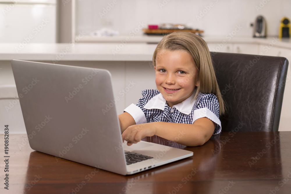 young beautiful and sweet little girl 6 to 8 years old with blond hair and blue eyes sitting at home kitchen enjoying with laptop computer smiling happy young beautiful and sweet little girl 6 to 8 years old with blond hair and blue eyes sitting at home kitchen enjoying with laptop computer smiling happy