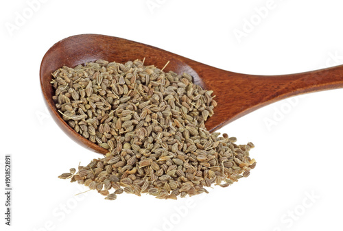 Pile of dried anise seed with wooden spoon on a white background