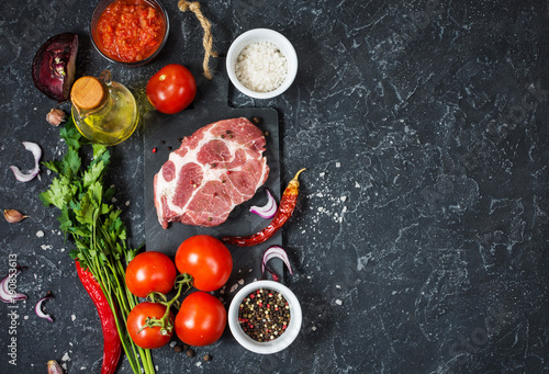 Raw marbled meat steak with ingredients for cooking on dark stone background