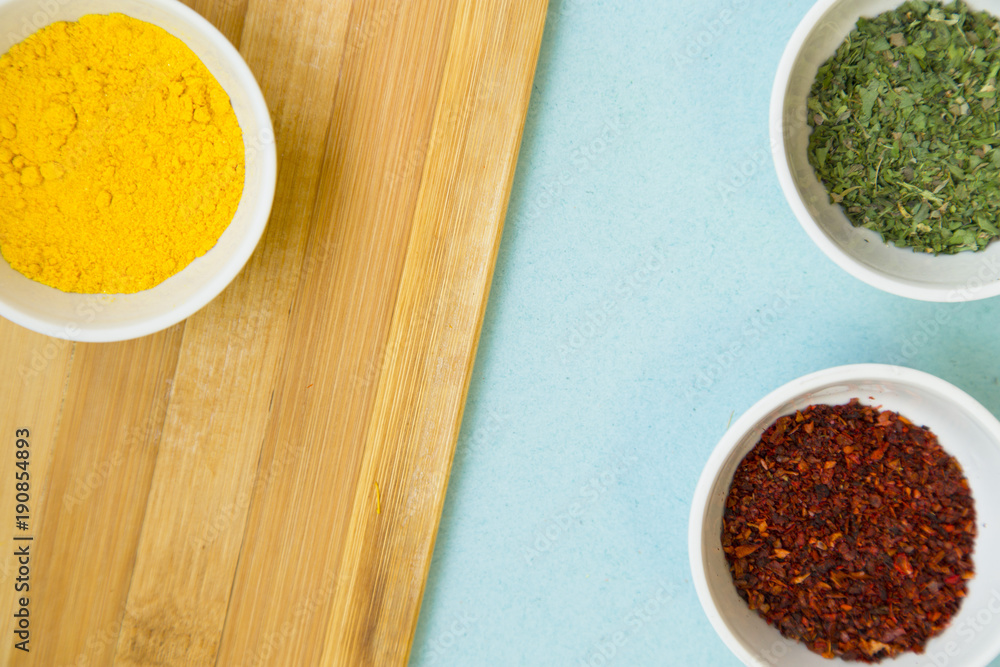Plastic cups with dry spices and fresh herbs on a wooden cutting board with blue background, top view, close up Plastic cups with dry spices and fresh herbs on a wooden cutting board with blue background, top view, close up
