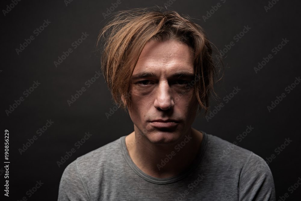 Portrait of exhausted sad guy with shaggy hair standing and looking at camera with apathy. Isolated on background Portrait of exhausted sad guy with shaggy hair standing and looking at camera with apathy. Isolated on background