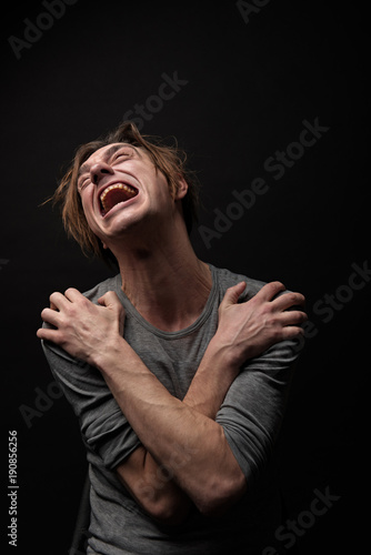 Canvas-taulu Waist up portrait of frustrated junkie sitting with arms crossed on chest, he is looking up and crying