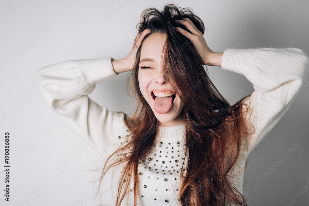 Funny cheerful woman shows tongue with eyes closed, shouting, fooling around, making a grimace. Positive emotions.