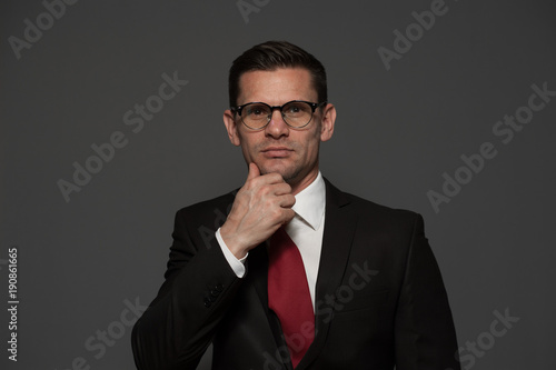 Portrait of an successful happy businessman in formal suit and glasses looking at the camera posing on gray background