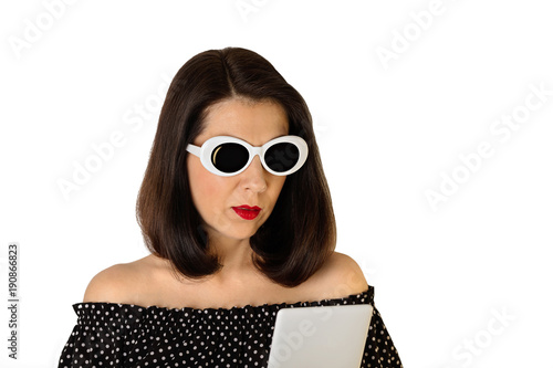 Woman in a black and white dress with polka dots and white sunglasses holding an electronic book  tablet .