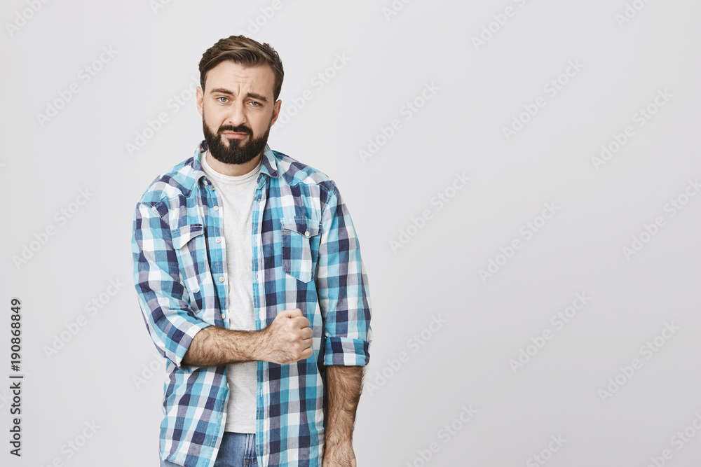 Attractive bearded european man with gloomy smile, squeezes fist, expressing tiredness and unwillingness to action, standing over gray background. Person is overloaded with work but should keep up Attractive bearded european man with gloomy smile, squeezes fist, expressing tiredness and unwillingness to action, standing over gray background. Person is overloaded with work but should keep up