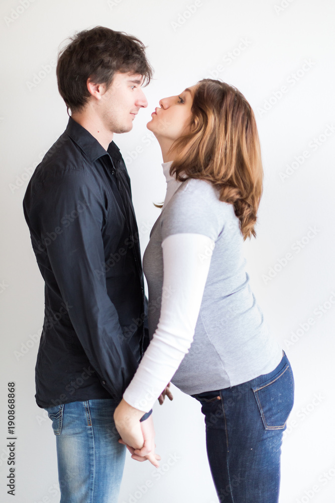 pregnancy, feelings, care concept. there is a loving couple, they are having some fun and playing with each other, she is wearing gray sweater and jeans and he is in the shirt and jeans