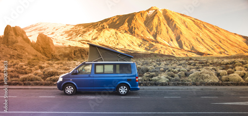 Small travel vehicle camping van or big car with folding rooftop with bed is parked under huge mountain formation. Tourism vacation and travel. Camper van and mountains landscape