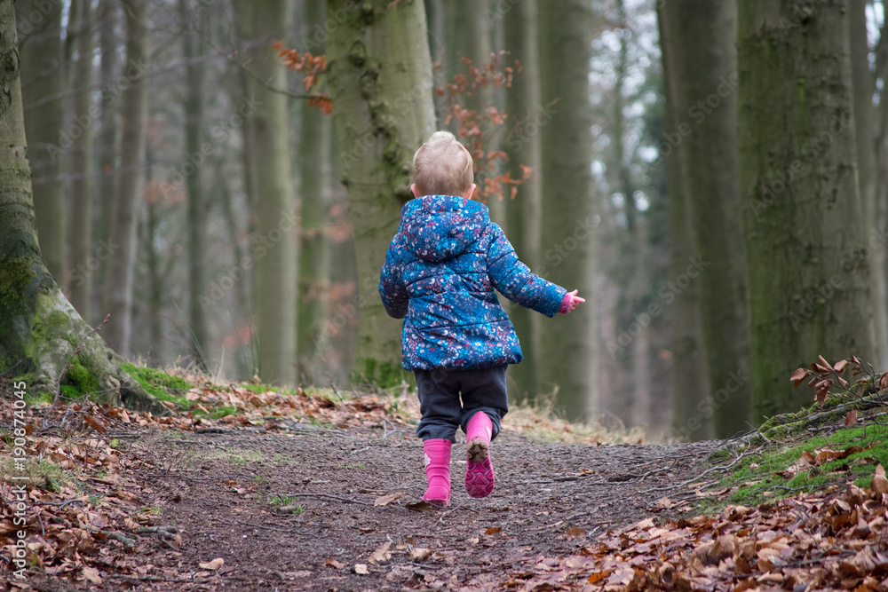 Little girl climbing a small hill. Wearing blue jacket and pink boots.