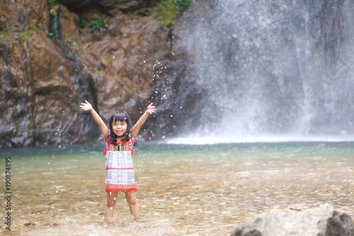 Asian children cute or kid girl smile with fun and enjoy playing water splash on waterfall and holiday relax trip for summer at Jokkradin waterfall