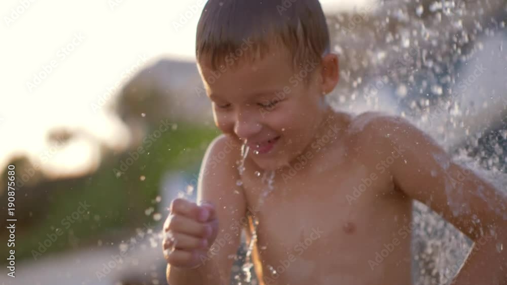 Slow motion shot of a joyful kid having fun when taking outdoor beach shower. Laughing child dancing and splashing water Slow motion shot of a joyful kid having fun when taking outdoor beach shower. Laughing child dancing and splashing water