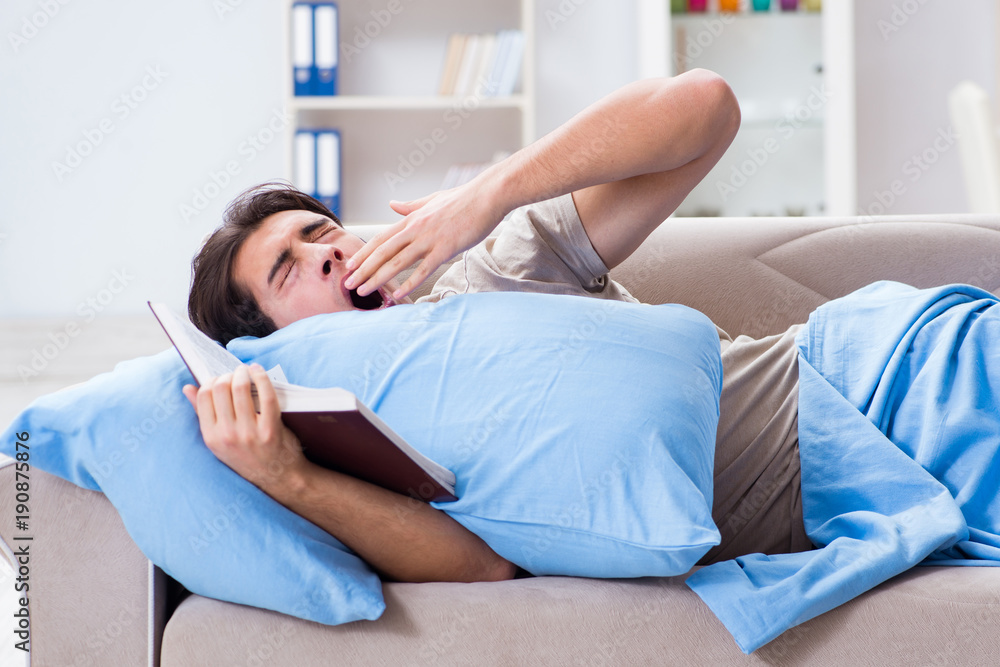 Young student man preparing for college exams in bed with book Young student man preparing for college exams in bed with book