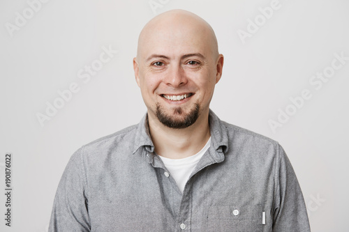 Close-up portrait of happy bald european with beard expressing confidence and reassurance, standing over gray background. Mature man started business with his old friend, feeling it will be successful