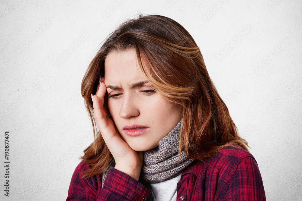 Illness and sickness concept. Exhausted stressed young female suffers from migraine, keeps hand on head, looks desperately down, isolated over white background. Woman has terrible headache Illness and sickness concept. Exhausted stressed young female suffers from migraine, keeps hand on head, looks desperately down, isolated over white background. Woman has terrible headache