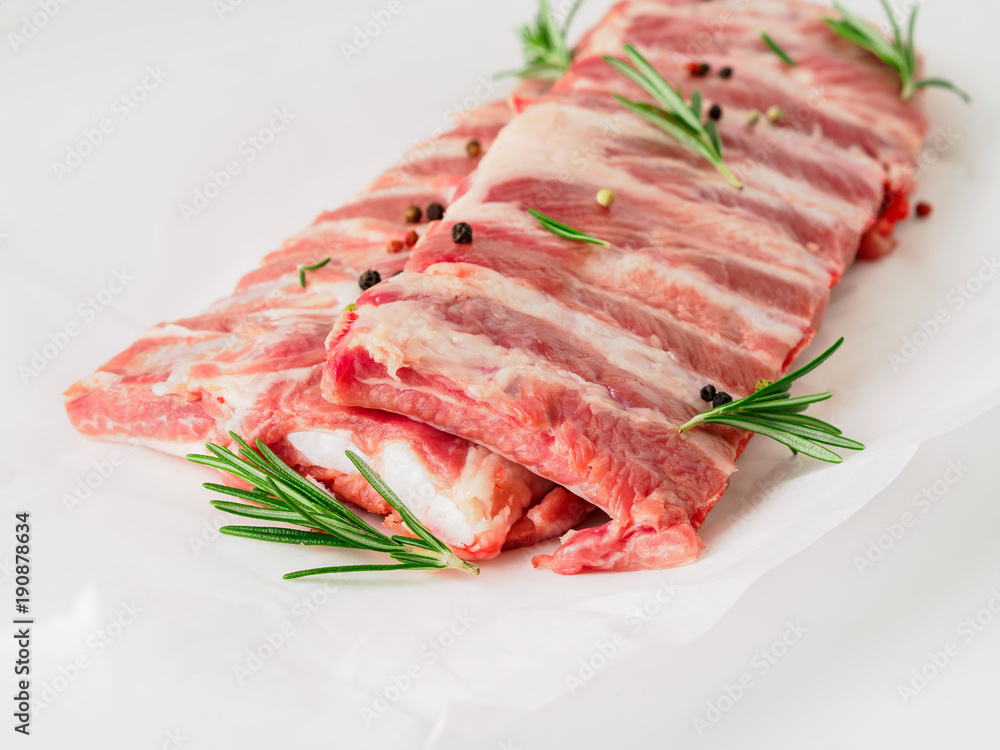 raw pork ribs with seasoning rosemary, pepper on white parchment paper, side view raw pork ribs with seasoning rosemary, pepper on white parchment paper, side view