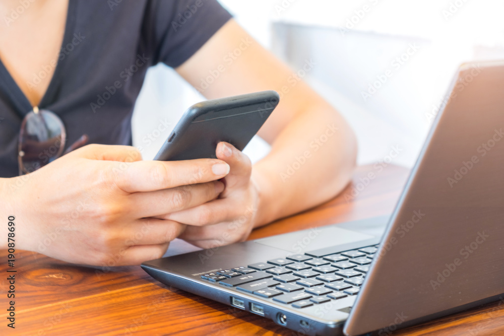 Fototapeta premium Woman playing a smart phone with laptop placed in front.
