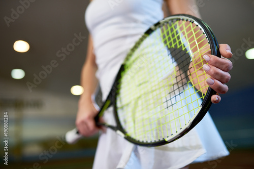 Close up of unrecognizable young woman holding tennis racket while playing in indoor court, copy space © Seventyfour