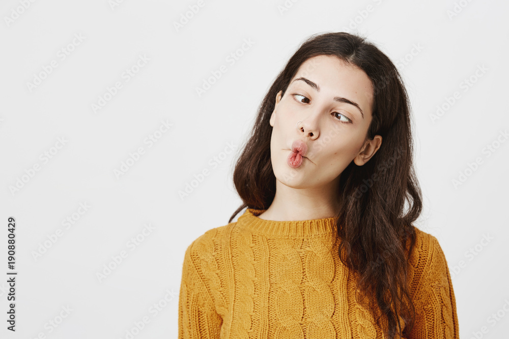 Indoor shot of funny childish woman with pierced nose making crazy eyes and fish lips while Indoor shot of funny childish woman with pierced nose making crazy eyes and fish lips while