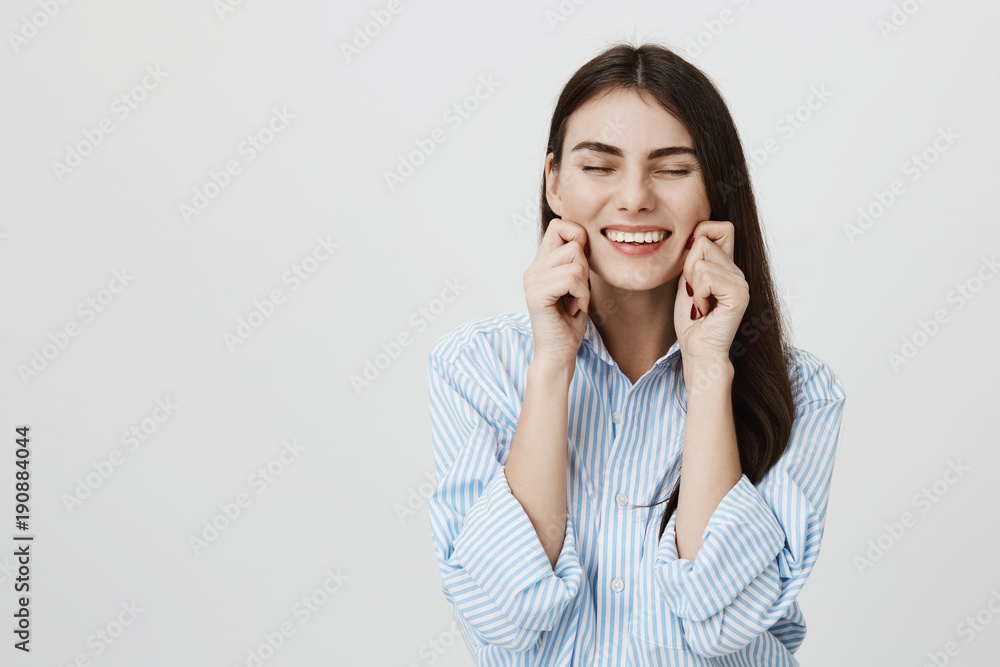 Happy and sincere woman stretching cheeks and smiling brightly while standing over gray background. Adult coworker after feels relieved and great after visiting spa salon Happy and sincere woman stretching cheeks and smiling brightly while standing over gray background. Adult coworker after feels relieved and great after visiting spa salon