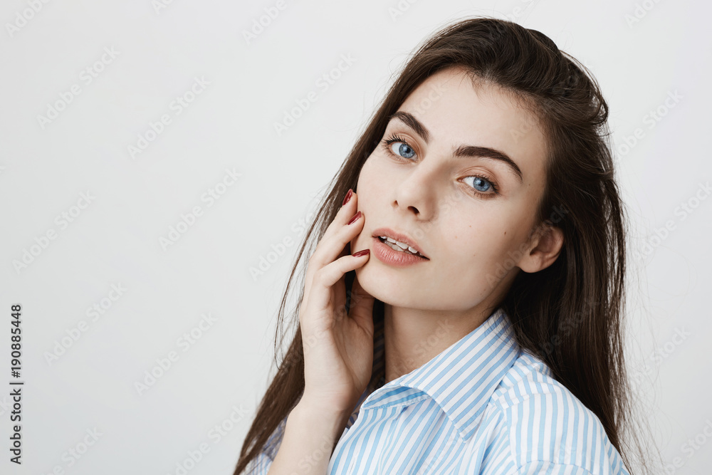 Close-up portrait of sensual and tender adult woman holding hand on face and looking dreamily at camera while standing over gray background. Cute female make-up artist shows master class Close-up portrait of sensual and tender adult woman holding hand on face and looking dreamily at camera while standing over gray background. Cute female make-up artist shows master class