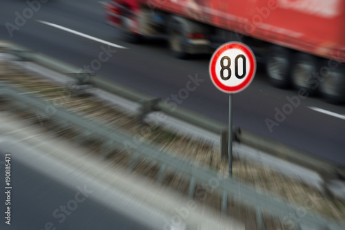 Defocused image of traffic sign showing speed limit on a highway with truck driving in the background