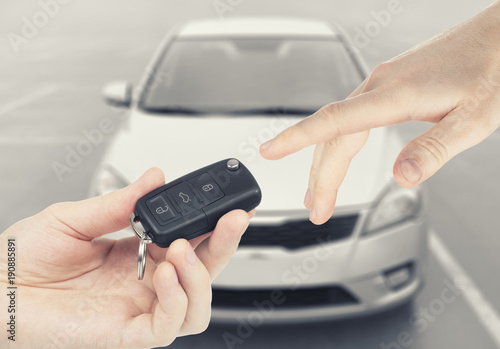 One person passing car keys to another person with car on background